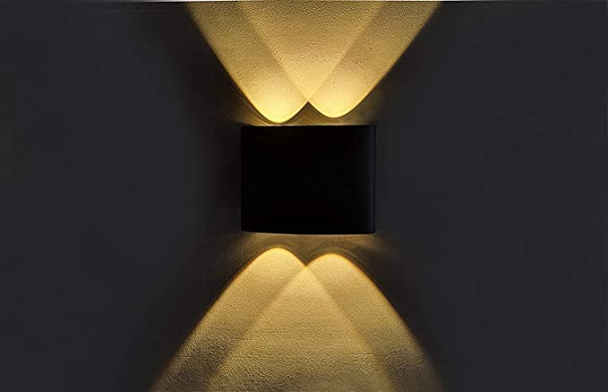 A modern black rectangular wall sconce emitting warm yellow light in two symmetrical upward beams against a dark gray wall.