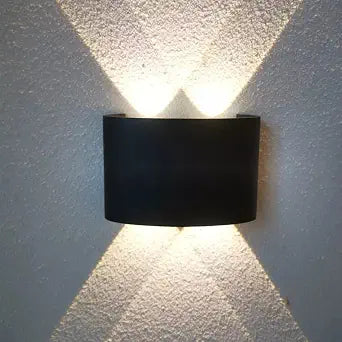 A modern black wall-mounted light fixture casting a symmetrical dual-cone light beam onto a textured white wall.