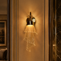 A modern wall sconce with a gold-finished metal fixture and a spiral glass shade that diffuses warm light, mounted on a beige paneled wall in an elegant interior setting.