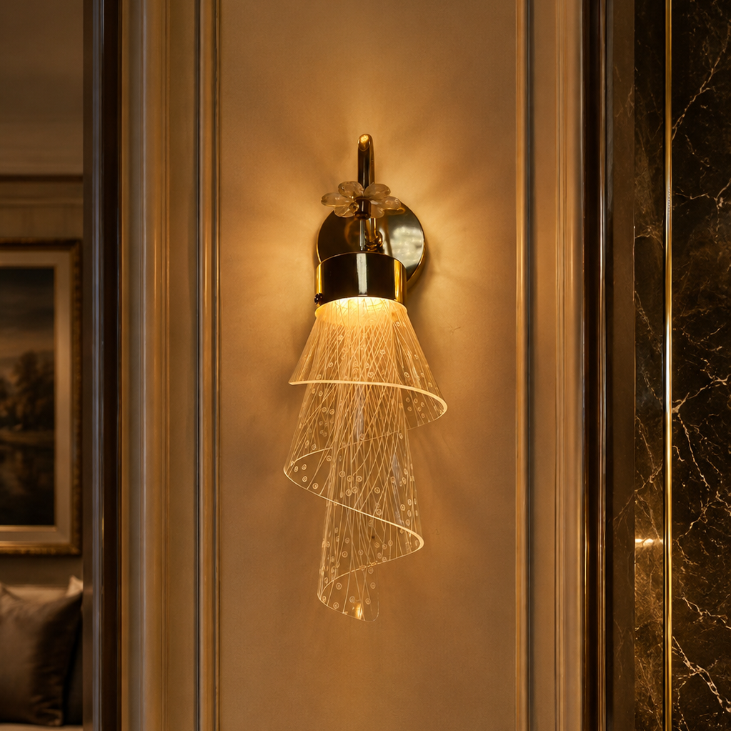 A modern wall sconce with a gold-finished metal fixture and a spiral glass shade that diffuses warm light, mounted on a beige paneled wall in an elegant interior setting.